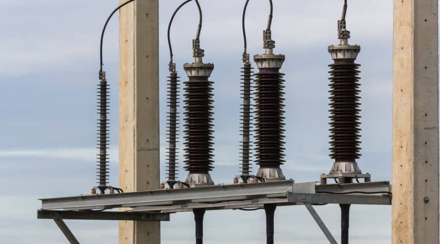 A row of high-voltage lightning arresters installed on a power transmission system. The devices feature stacked ceramic or polymer insulators and are connected to overhead power lines.