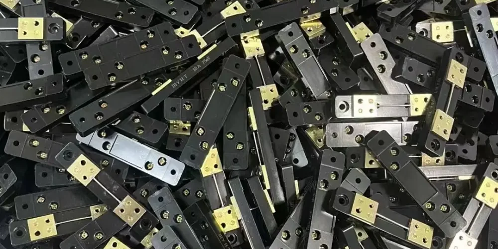 This image shows a pile of DC shunt，which are likely used in electrical applications for measuring current. Each piece has a black insulating base and is fitted with two metal plates, likely made of brass, for conductivity.